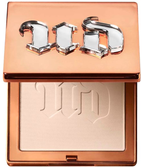 A compact with a shiny copper-colored lid displaying bold metallic letters 'Dior' and a light beige pressed powder inside.