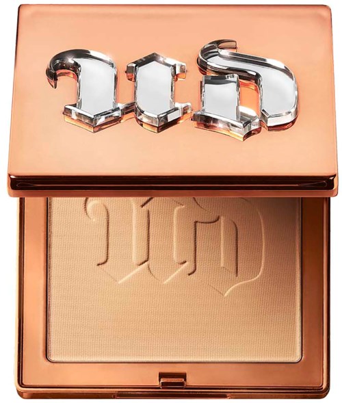 A compact with a rose gold lid and reflective letters spelling 'IED'. The inside shows a light beige powder with embossed design.