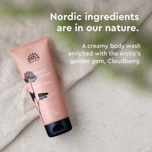 En rosa kroppstvätt förpackning med texten 'Creamy Body Wash' och bilder av svarta och vita bär, placerad på mjukt tyg.