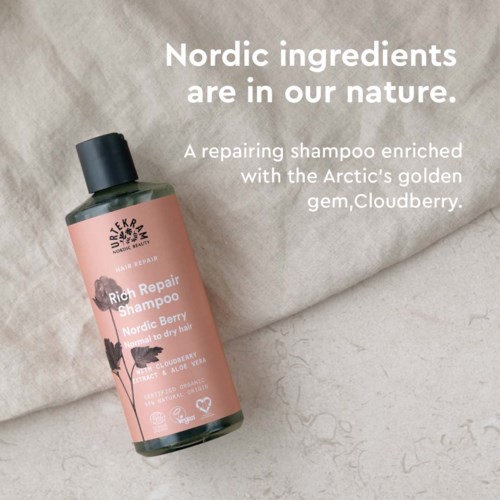En rosa flaska med Rich Repair Shampoo på ett beige tyg med text om nordiska ingredienser och arktiska bär.