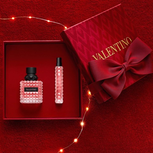 Two pink Valentino perfume bottles in a red gift box with a bow, surrounded by fairy lights on a red background.
