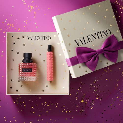 Ein Valentino-Geschenkset mit Parfümflasche, rosa Armband und Box mit violetter Schleife auf lila Hintergrund.