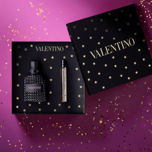 Valentino perfume gift set with a bottle and an additional item in a starry box. Pink background with gold confetti.
