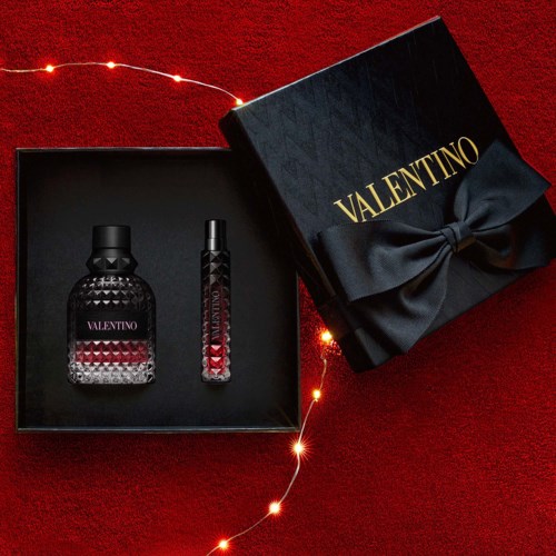 Valentino perfume gift set with two bottles in a black box with a bow, on a red background with fairy lights.