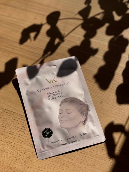 En påse med ansiktsmask som visar en kvinna med stängda ögon och ett lugnt leende, solljus och skuggor på den.