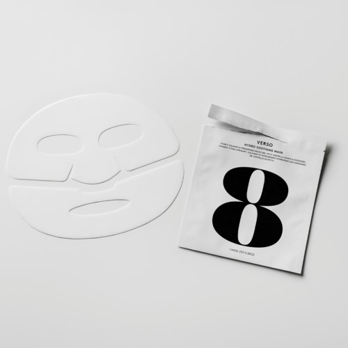 En vit ansiktsmask och ett paket med en svart och vit abstrakt design ligger på en vit yta.