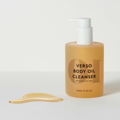 En flaska Verso Body Oil Cleanser med vätska som spillts bredvid mot en enkel bakgrund.