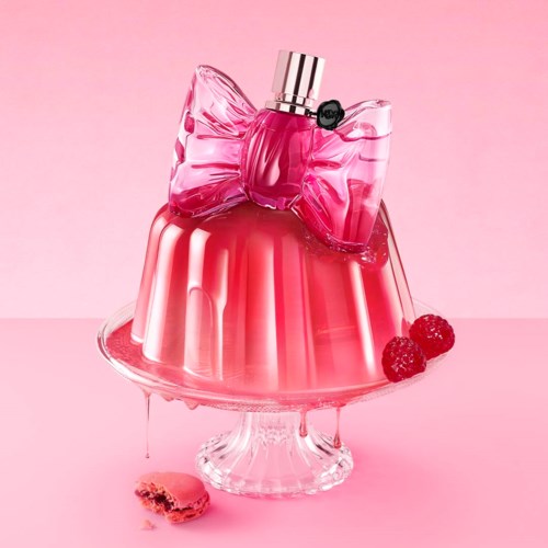 A pink and red jelly dessert with a large bow-shaped decoration and raspberries, in a clear glass dish.