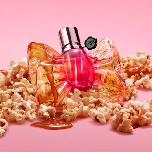 A perfume bottle surrounded by popcorn on a pink background.