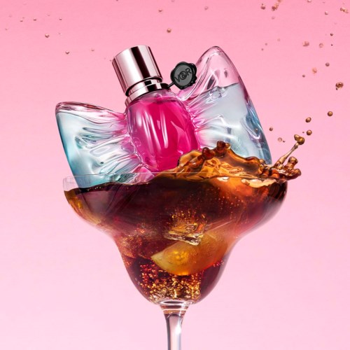 Pink perfume bottle in a glass with splash of liquid, against pink background, with gold glitter.
