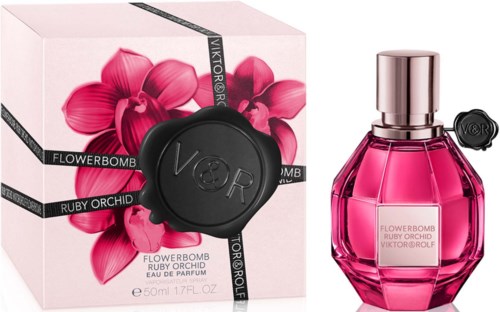A pink perfume bottle with a shiny cap beside a box decorated with pink orchids and black ribbons.