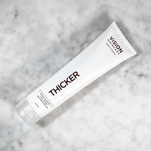 Eine weiße Tube mit der Aufschrift 'THICKER' von Vision Hair Care, auf einer hellgrauen Steinoberfläche.