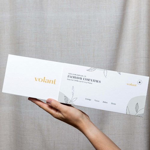 A hand holds a white box with leaves and text about essential oils and relaxation.