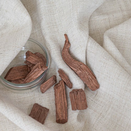 Pieces of brown bark-like material spilled on a soft beige fabric, with a small glass container nearby.