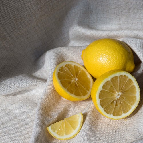 Two whole lemons and two lemon halves with a slice are on a cloth background.