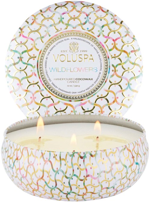 Et dekorativt stearinlys med tre flammer i en rund, mønstret eske med teksten "Voluspa Wildflowers."