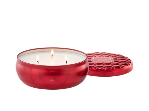 Red candle holder with three lit wicks and a decorative lid nearby.