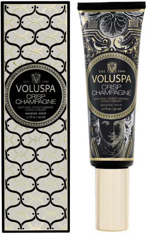 Een zwart en goud gestileerde doos en een zwarte tube met vergelijkbaar ontwerp, beide zijn cosmetica producten met label 'Voluspa Crisp Champagne.'