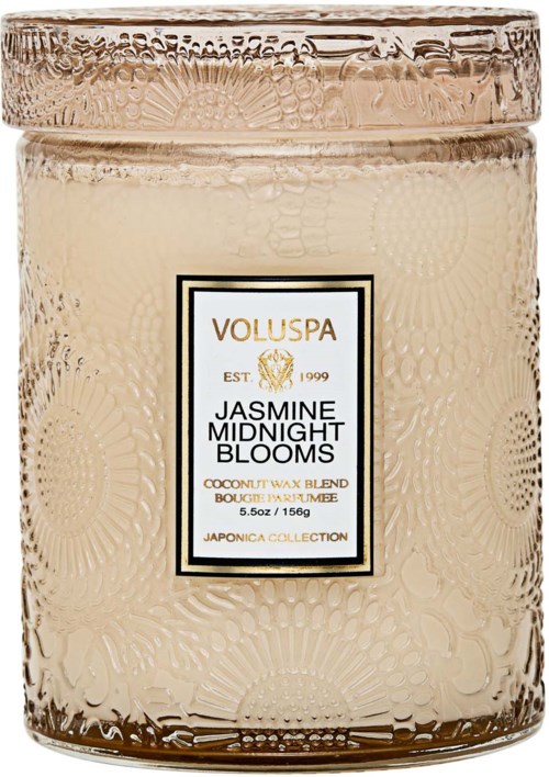 Ett ljus i ett glas med en texturerad yta och en etikett som säger 'Jasmine Midnight Blooms' och 'Voluspa.'