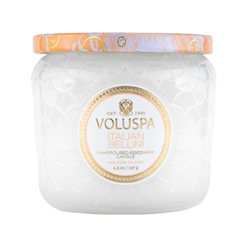 Een witte kaars in een glazen pot met een decoratief goud- en oranje etiket en deksel.