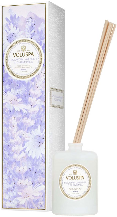 Een witte fles met deksel en stokjes erin, naast een lange doos met paarse bloemendesign en etiket.