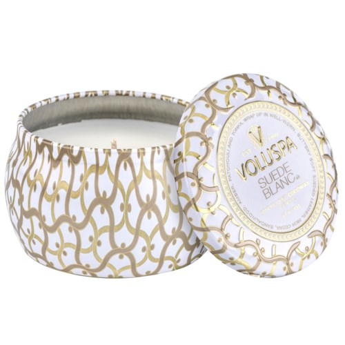 Een ronde witte en gouden container met een deksel, met de tekst "Voluspa Suede Blanc". Het lijkt een geurkaars of cosmetisch product.