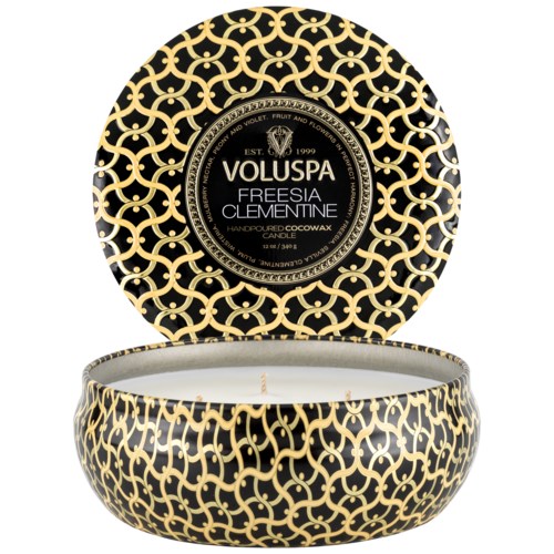 En rund svart och gyllene mönstrad ljusbehållare med lock, märkt Voluspa Fresia Clementine.