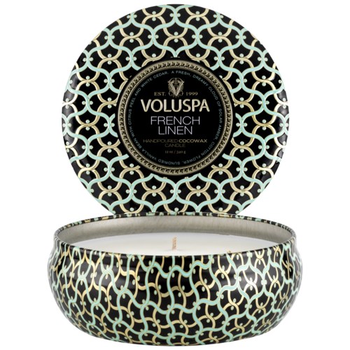 En rund lysfat med svart og gullig komplisert mønster, etiketten sier 'Voluspa French Linen'.