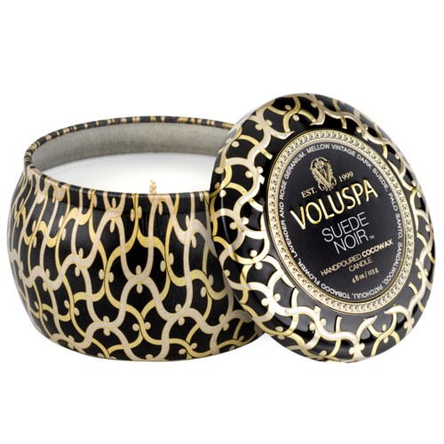 Een decoratieve kaars met zwart en goud patroon en een deksel. Het etiket zegt dat het een suede noir geurkaars is.