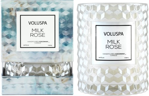 Två dekorativa ljus med geometriska mönster, ett i blått och silver, det andra i vitt, märkta 'Voluspa Milk Rose' och tillverkade i USA.