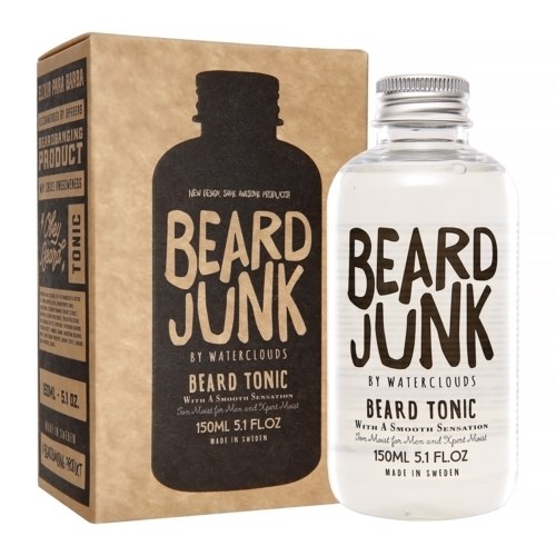 Een heldere fles en een-bruin doos, beide gelabeld "Beard Junk" baard tonic, met zwarte en witte tekst, in een winkelomgeving.