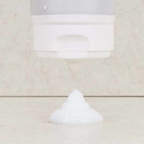 Vitt skum kommer ut från en väggmonterad dispenser på en yta.