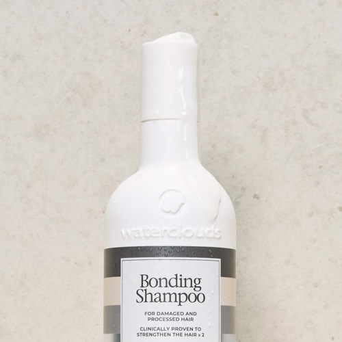 En hvit flaske med pumpe, merket 'Bonding Shampoo', for skadet hår, med grå og svart etikett.