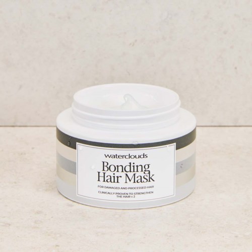 En hvit beholder av Waterclouds Bonding Hair Mask med svarte og sølvstriper, delvis åpen og viser kremen inni.