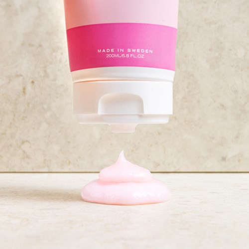 Ett rör i rosa och vitt som trycker ut rosa kräm på en plan yta.