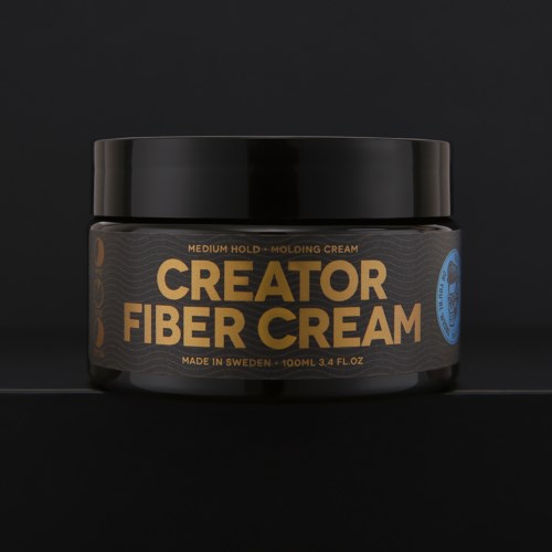 Een zwarte pot met label 'Creator Fiber Cream' met goud en blauw details, op een zwarte achtergrond.