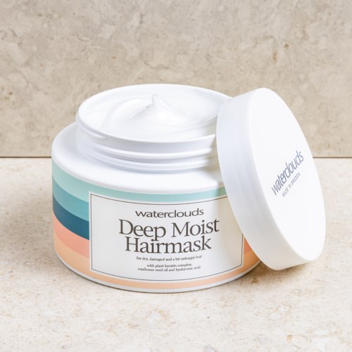 En rund beholder med dyb fugtgivende hårmaske med hvid creme indeni, mærket "Waterclouds" på en beige overflade.