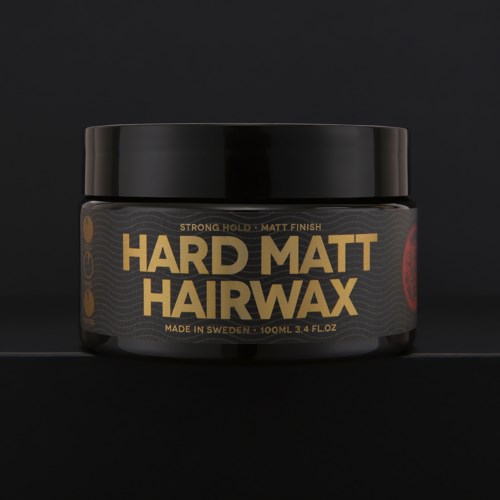 Ein schwarzer Behälter mit Hard Matt Hair Wax mit goldfarbenem und rotem Text und Design auf dunklem Hintergrund.