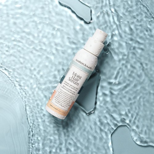 En vit flaska märkt 'Moist Hair Serum' ligger på en texturerad, iskall blå yta med isbitar runt den.