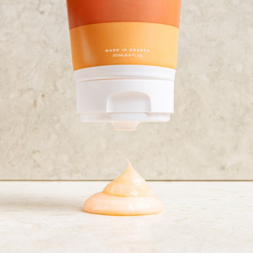 Ett rör som pressas ut, släpper en virvel av orange kräm eller lotion på en yta.