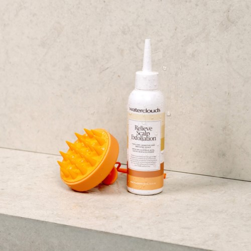 Eine Flasche mit Kopfhautpeeling und eine gelbe Massagebürste auf einem Badezimmer-Tablett.