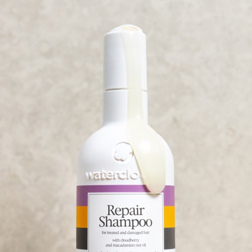 Hvid flaske med Repair Shampoo til skadet hår, med lilla, gul og sort stribe.