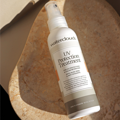En vit sprayflaska märkt 'waterclouds UV Protection Treatment' med orange och grå accenter, placerad på en beige yta.