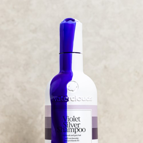 En hvit flaske med lilla detaljer merket Violet Silver Shampoo for hårpleie og fargeskjerming.