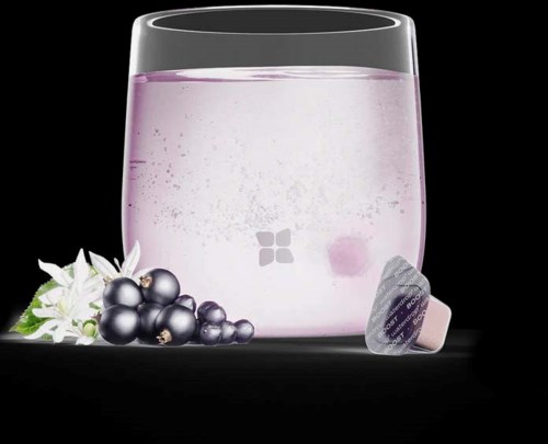 A glass with purple liquid, coffee pods, grapes, and white flowers beside it on a black background.