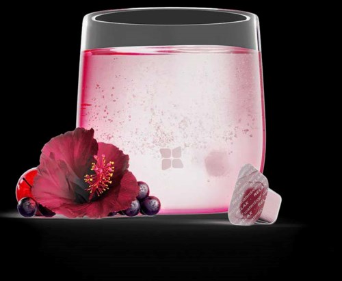 A glass with pink liquid, a hibiscus flower, berries, and a candy on a black background.
