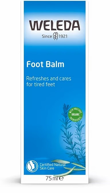 Blå och vit förpackning för Weleda fotbalsam, med örtillustration och text om naturlig hudvård.