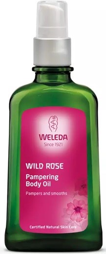En grön flaska med Weleda Wild Rose body oil med vit pump, etikett med produktnamn och beskrivning.
