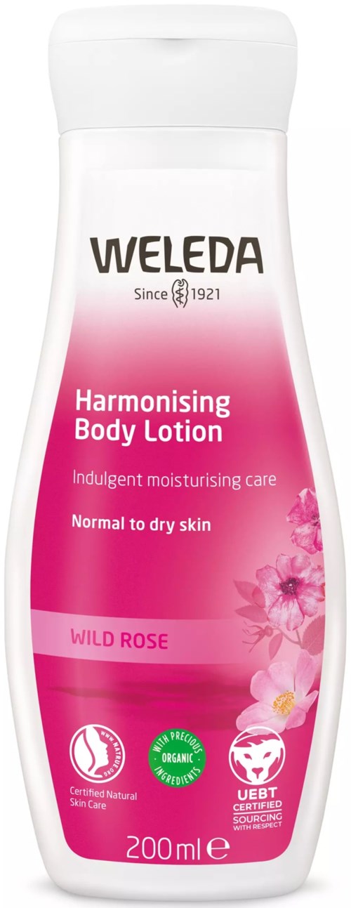 En vit och rosa flaska med Weleda kroppslotion för normal till torr hud, med doft av vildros och flera certifieringslogotyper.