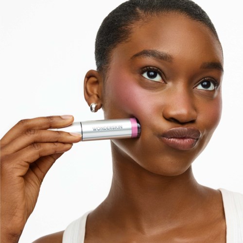 Woman holding a silver and pink WonderSkin makeup product near her cheek.
